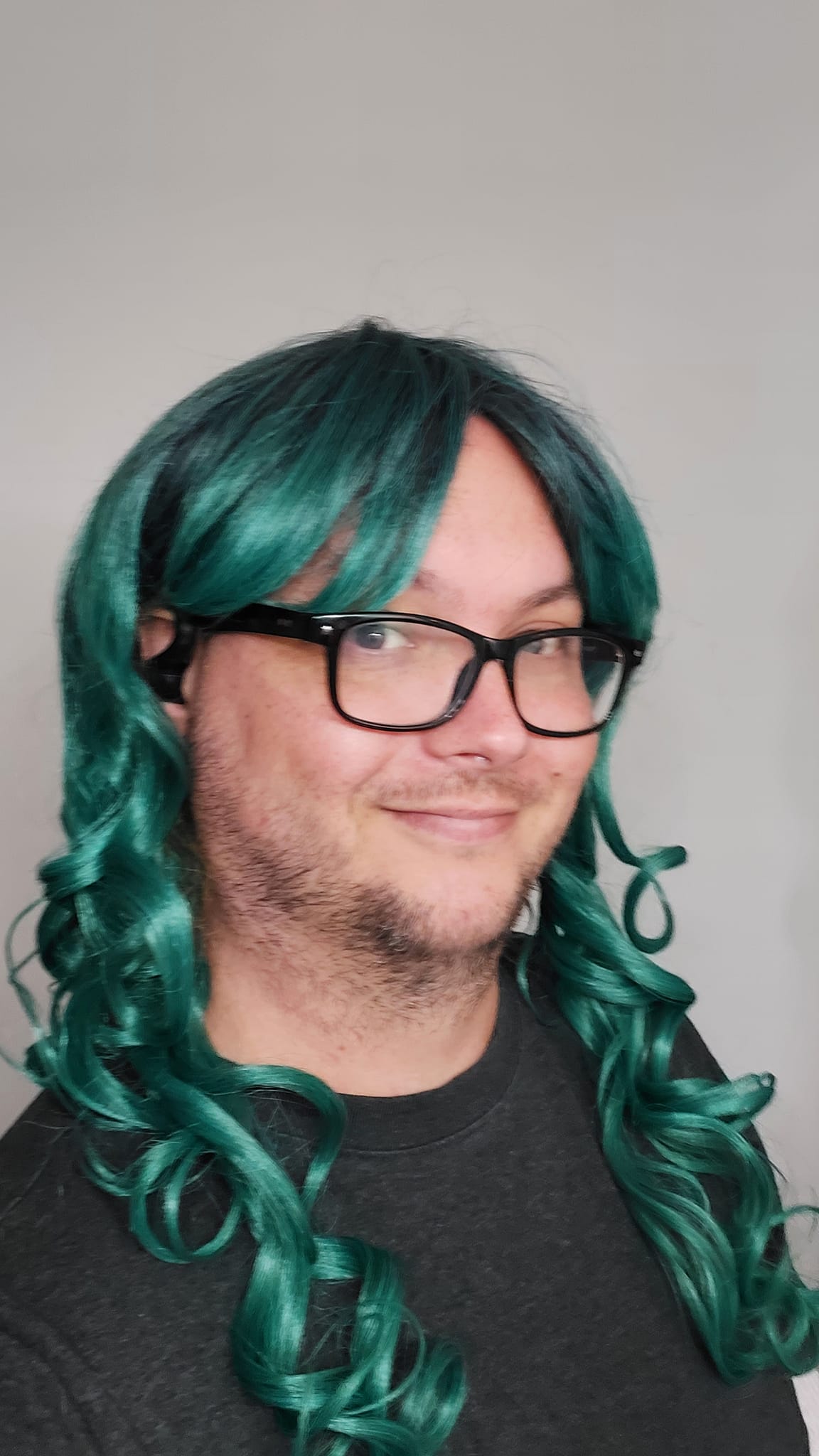 A man wearing a black shirt wears a long teal curly costume wig